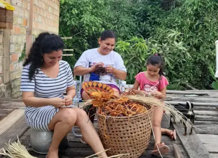 Mãe, filha e neta trançam palha de tucumã no Rio Arapiuns.