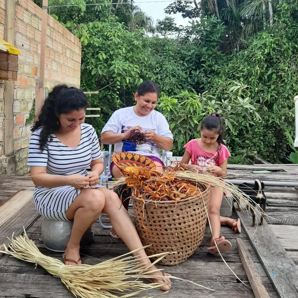 Mãe, filha e neta trançam palha de tucumã no Rio Arapiuns.